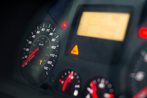 A close-up view of a car dashboard showing the speedometer, warning lights, and various indicators, with a focus on the speed and caution symbols.