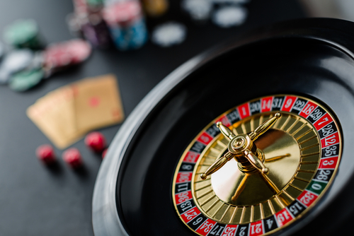 A close-up of a spinning roulette wheel with poker chips and playing cards blurred in the background, representing the casino environment.