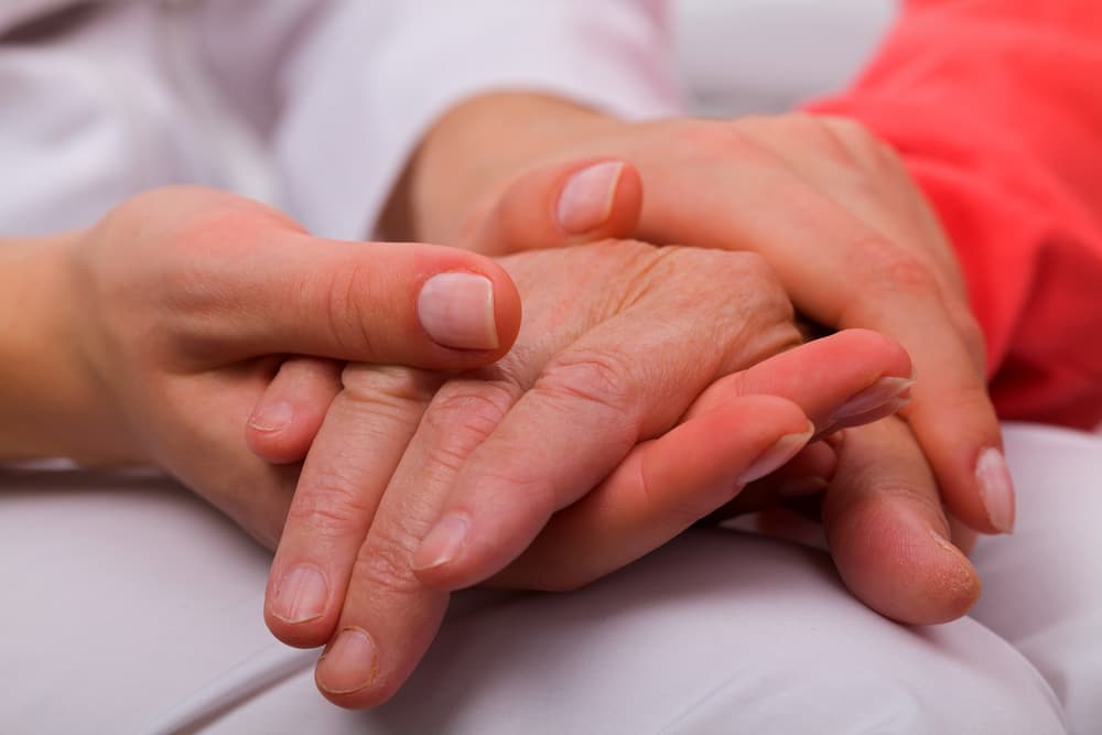 Caregiver holding elderly patient's hand at home