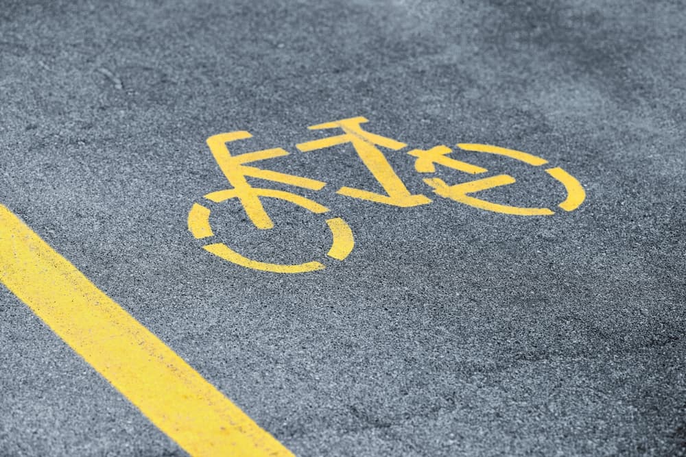 Yellow bicycle sign on cycling path, safe road traffic near highway.